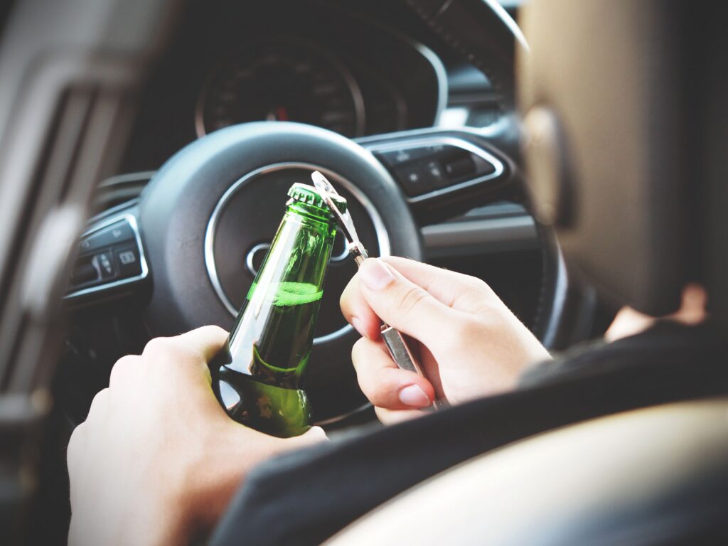 Driver's seat of cat, hands opening bottle of beer in front of steering wheel