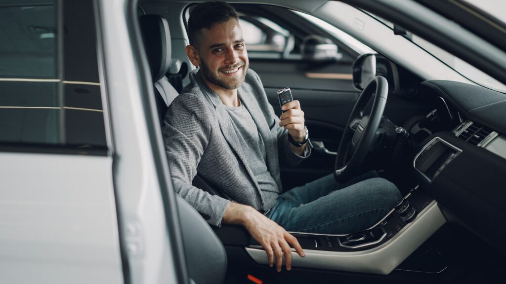 Man in driver's seat of car holding up key and smiling