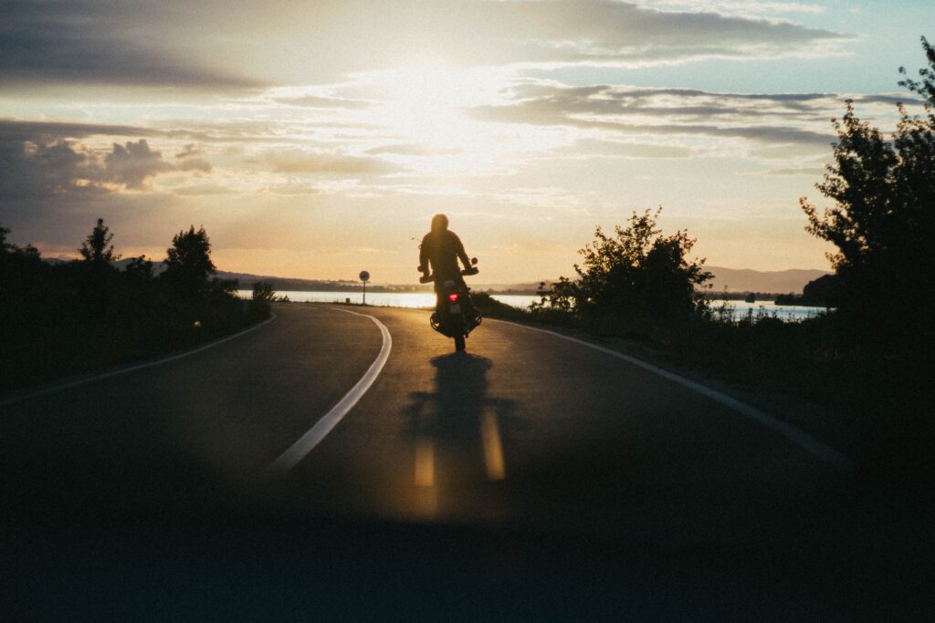 A biker riding his motorcycle on the highway while the sun is setting.