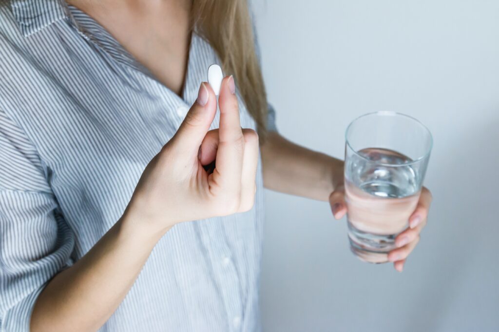 A woman holding a medication tablet in one hand and a glass of water in the other.