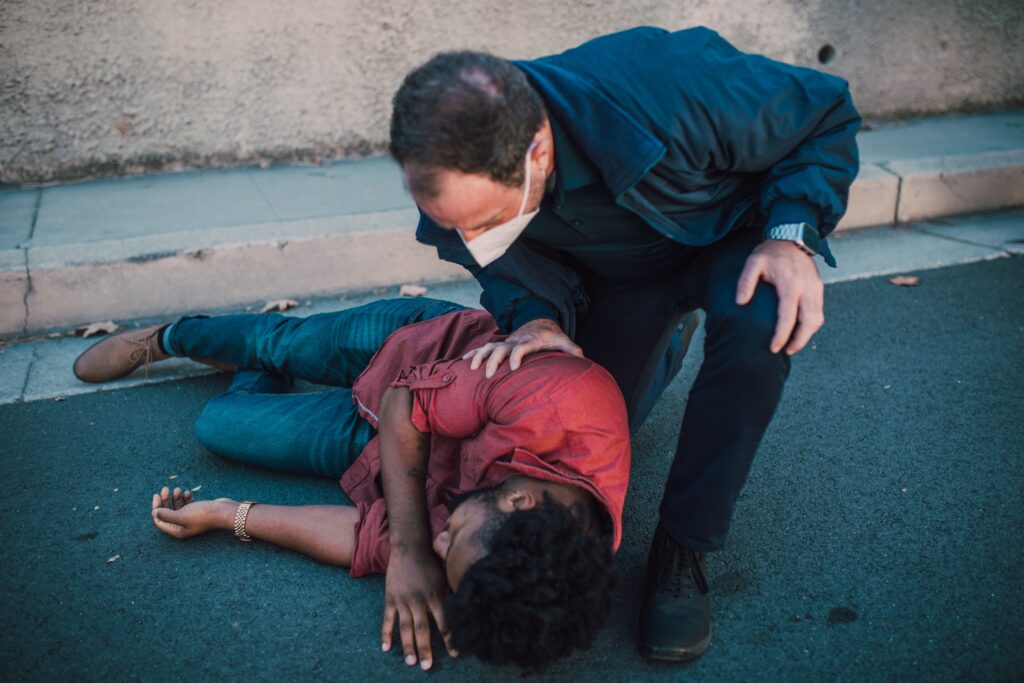 Man on ground in pain with another man in mask kneeling down to check on him