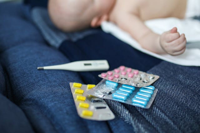 pill blister packs and a thermometer next to a sick infant