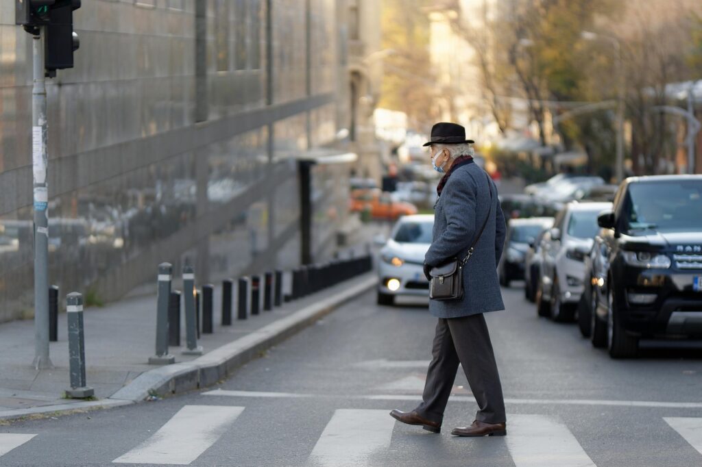 Elderly man in hat and winter coat crossing street at crosswalk in front of oncoming car