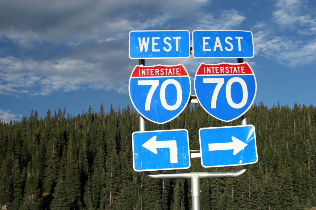 Road sign with east and west interstate 70 directions backed by trees